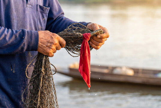 Fisherman's aged hands holding a wet cast net over water