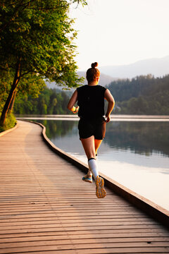 Woman running by the lake on a sunny day. Active lifestyle and outdoor fitness concept.