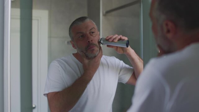 Man using electric razor trimmer to shave beard in bathroom, 4k