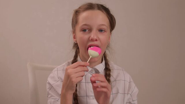 Girl sampling vibrant candy joyfully. Youthful girl indulges in colorful treat happily. Child with braided hair tastes bright pink candy with curiosity and delight