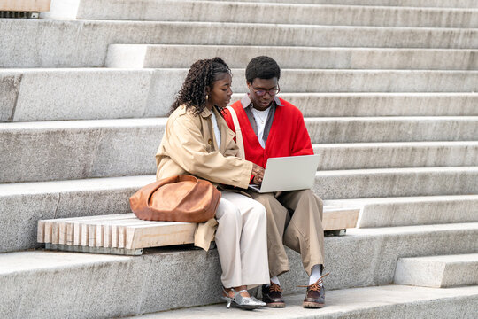 Nerdy focused black man student explaining studies on laptop to black woman friend while sitting outdoors, intellectual african american students friends chatting about lessons and university projects
