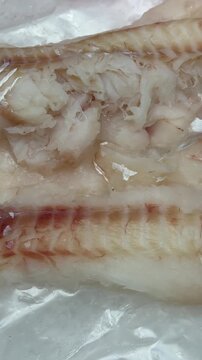 Fresh cod fillets on ice display, trimmed pale pink flesh arranged on crushed ice at seafood market counter