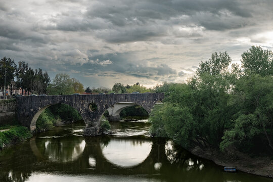 Roman stone bridge over the Volturno River in Capua with a cloudy sky. Ideal for tourism promotion, editorial content about the Caserta area, or conceptual design.