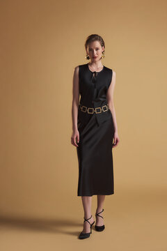 Woman in black sleeveless midi dress with belt on beige background
