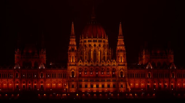 Hungarian parliament building glowing orange at night in Budapest. Majestic facade of Budapest&rsquo;s hungarian parliament illuminated in warm golden-orange light against the dark night sky