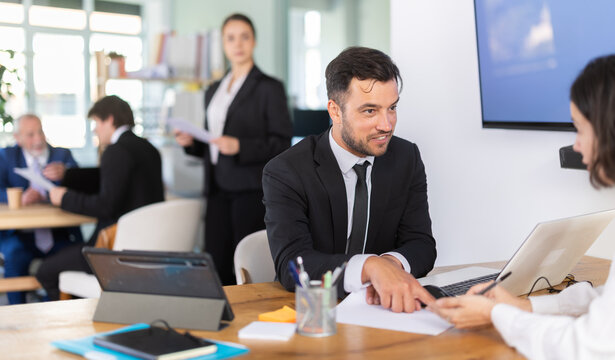 Professional adult male lawyer or bank employee talking and signing loan agreement with young woman client in modern bank