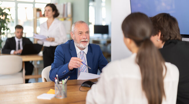 Elderly male bank employee at desk with laptop and discussing with young couple customers