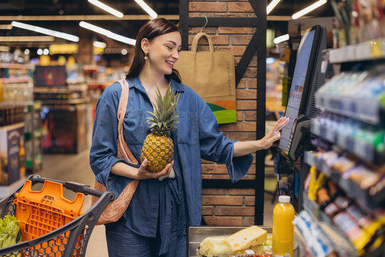 Woman scanning fresh pineapple at self checkout in modern grocery store, managing shopping and payment process