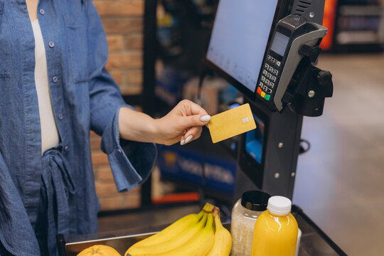 Woman paying for groceries, using a golden credit card for contactless payment at a supermarket checkout