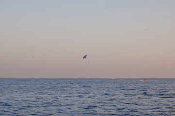 Naklejka premium Colorful kites dancing in breeze above calm Red Sea with distant sailing boats and sunset glow along Sinai coast. Parasailing and wind sports in peaceful evening atmosphere. Egypt coastal kite scene