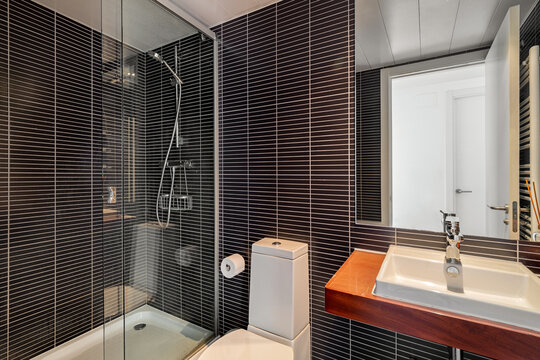Modern bathroom with a glass shower, sleek sink, and dark tiled walls. The space is well-lit and features contemporary design elements.