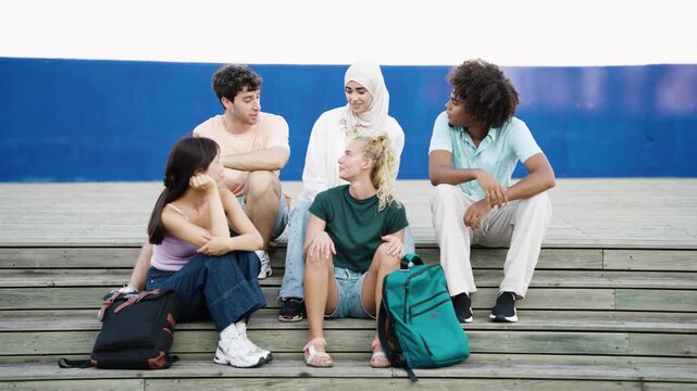 Multiethnic group of young friends having a conversation while sitting together on stairs outdoors. People from different cultures sharing time