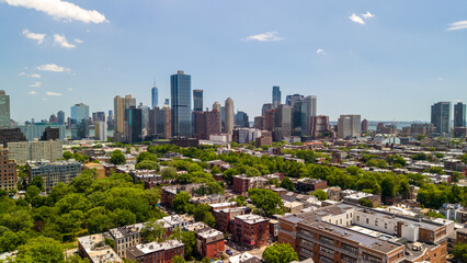 Fototapeta premium Jersey city downtown skyline with modern skyscrapers rising above tree lined brownstones and apartment blocks, showcasing a growing urban neighborhood and waterfront view