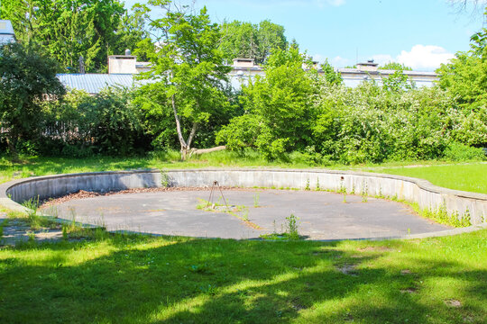 Warsaw, Poland, May 24, 2026. A large round concrete drainage or fountain base sits empty on a vibrant green lawn. High quality photograph.