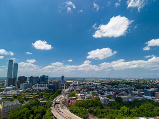 Obraz premium Jersey city urban landscape from an aerial perspective showing modern skyscrapers, a busy highway, and residential areas under a vivid blue sky with scattered clouds
