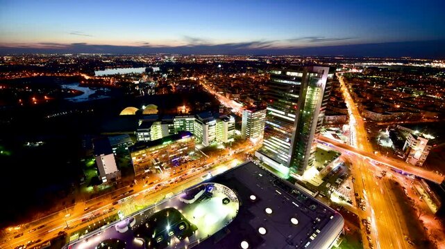 Bucharest, Romania - 26 September 2020: View of the illuminated modern skyline and glass office buildings with traffic on the streets at dusk.