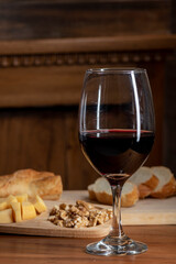 Naklejka premium Glass of red wine with bread and cheese on rustic wooden table