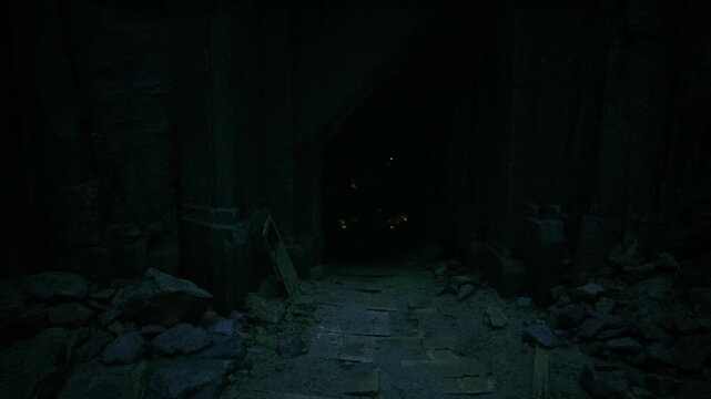 Lonely rocky path into dark interior, uneven floor strewn with stones leading toward distant tiny light, heavy shadows and cool blue tonal palette create