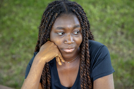 Pensive young African woman thinking in park, sad emotion outdoor portrait