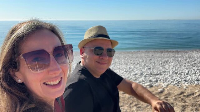 Pareja madura grabando selfie en la playa saludando
