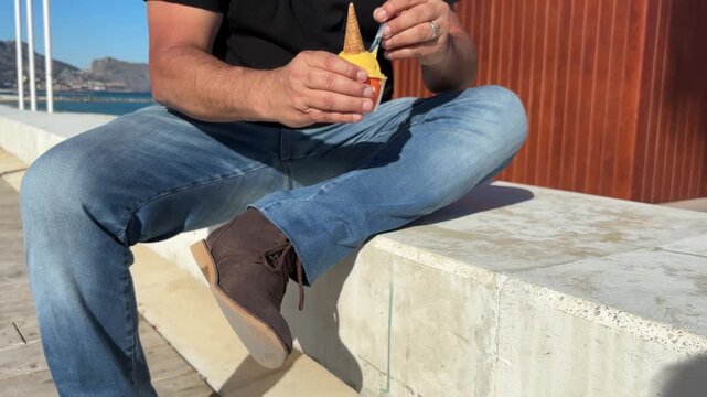 Hombre comiendo helado en paseo mar&iacute;timo sin rostro visible