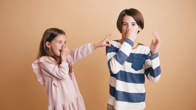 Brother and sister reacting to a terrible smell, plugging their noses with disgusted expressions. Playful children blaming each other for a stink