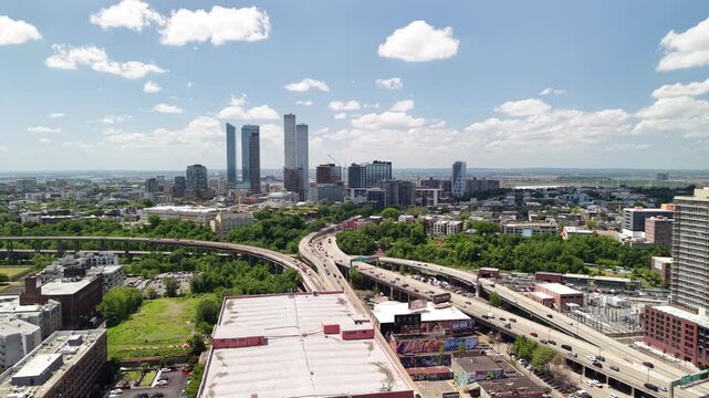 Aerial view of jersey city downtown skyline and highway traffic with skyscrapers, residential buildings and green urban park spaces under a beautiful cloudy summer sky