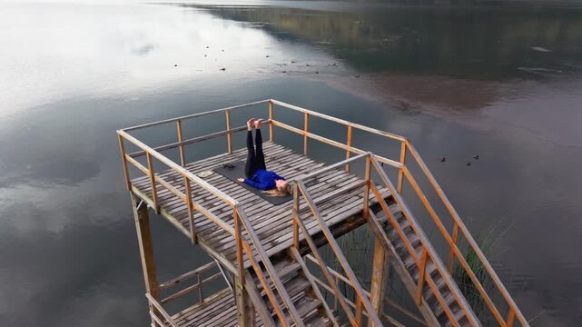 Athletic woman doing abs exercises on a wooden platform over the water at yahuarcocha lake, ecuador