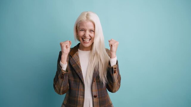 Cheerful young woman with long blonde hair expressing excitement and happiness. She is clenching her fists and celebrating a win
