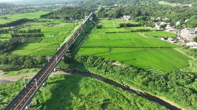 Aerial view of a high-speed bullet train crossing a river bridge amid green farmlands.