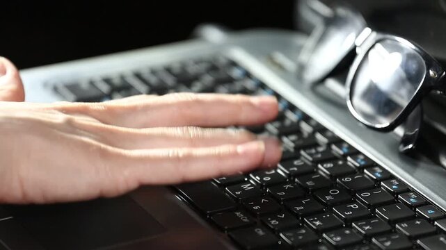 Business woman hands typing on a laptop with glasses on the keyboard. Online work, research on pc. Closeup workspace with person fingers
