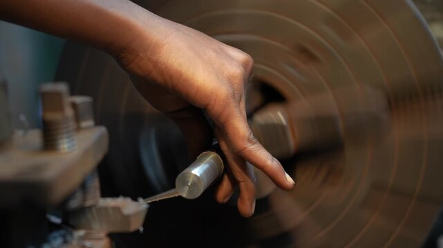 View of a worker's hand carefully operating a spinning metal lathe machine with metal shavings in Kushtia, Khulna Division, Bangladesh.