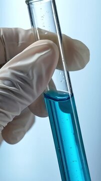 Gloved hand holding glass test tube with blue liquid solution