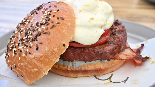 Gourmet beef burger with melted cheese sauce and crispy bacon on a sesame bun close up.