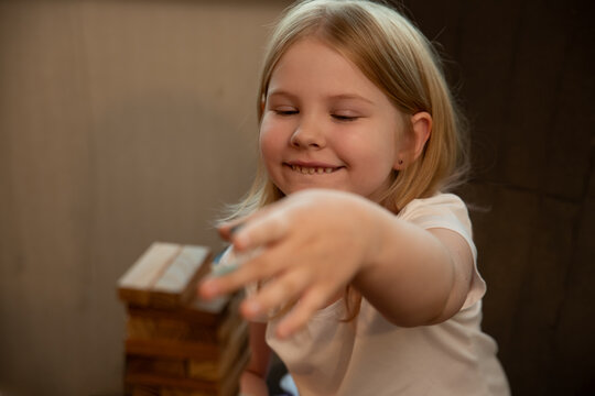 Young girl smiles while playing with wooden blocks. Real photograph of child focused on the game. Family activities and facial expressions. Selective focus.