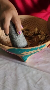 Close up of woman hands crushing garlic cloves and cumin seeds inside a volcanic stone molcajete