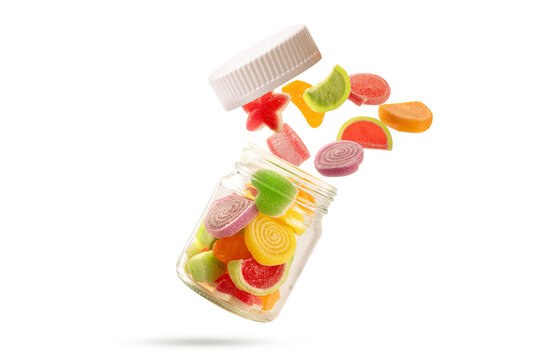 Levitating shot of assorted sugar-coated fruit jelly candies flying out of a glass jar with a white lid.  vibrant sweet snack concept isolated on white background.