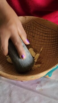 Close up of woman hands crushing garlic cloves and cumin seeds inside a volcanic stone molcajete