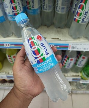 Kuala Terengganu, Malaysia - May 25, 2026: A person holding a plastic bottle of 100-Plus Reduced Sugar original carbonated isotonic electrolyte drink in a supermarket aisle.