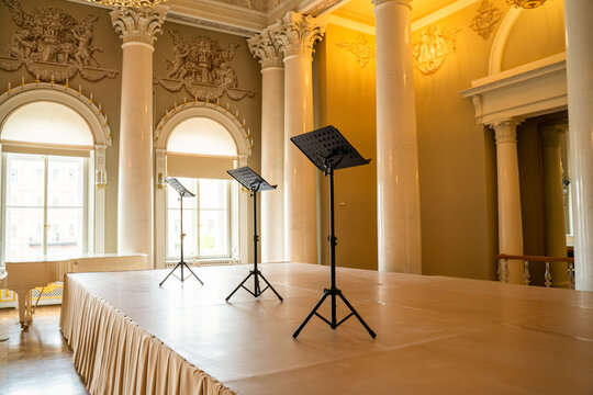 Opulent baroque concert hall interior with gilded column, arched window and black music stand on polished floor, luxury heritage venue concept.