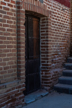 Muro y puerta de ladrillo rojo con puerta de madera con remaches, en calle con escalones.