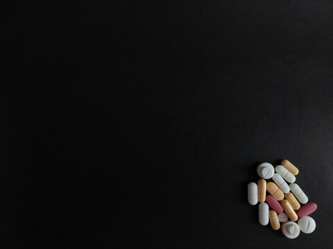 Assorted pills, tablets, capsules isolated on black background with copy space for drugs, medications, prescription medicines, medical treatments, vitamins, pharmaceuticals, and healthcare concepts.