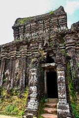Fototapeta premium Ancient ruined red brick Hindu temple tower with decorated columns and dark stone doorway at My Son Sanctuary in Vietnam