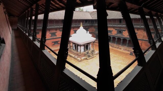 View of a traditional courtyard with a white shrine and ornate wood carvings from a balcony in Nepal.