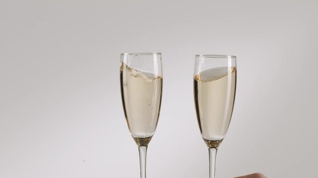 Champagne glasses toasting in a close-up studio shot. Two people clinking glasses of sparkling wine together in a celebratory toast, with the elegant champagne flutes isolated on white background