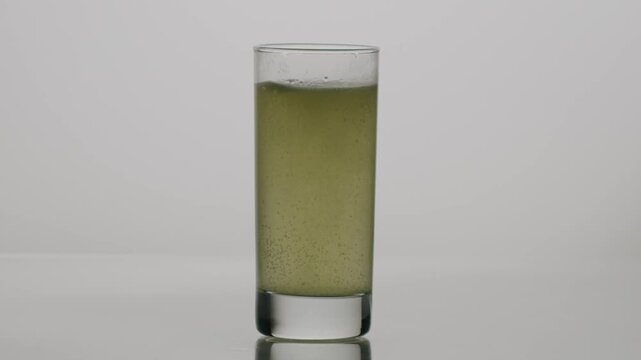Effervescent tablet dissolving in a glass of water, releasing bubbles in slow motion. Healthy nutritional supplement for hydration, vitamins, and minerals with a green tint.