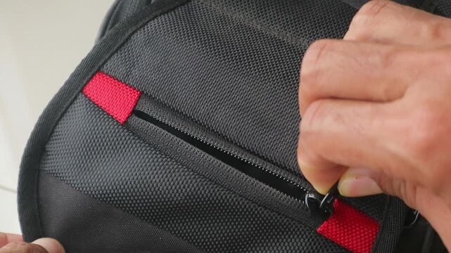Close up footage of hand opening the zipper on a black backpack with red details, showing travel, packing, storage and everyday use.