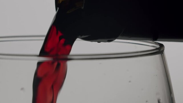 Elegant red wine pouring from the neck of a bottle into a crystal clear glass in super slow motion, highlighting the rich color and smooth flow of the beverage isolated on a white background