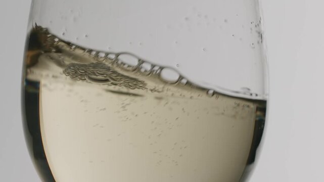 White wine swirling in a glass isolated on white background. Crystal clear glass filled with white wine swirling in slow motion, creating elegant waves and ripples on the surface of the golden liquid