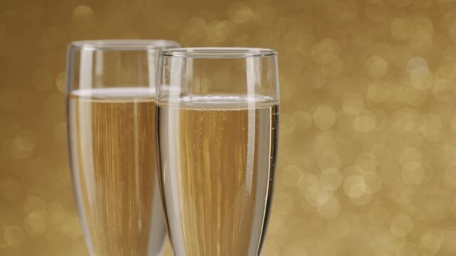 Sparkling champagne with rising bubbles in two elegant glasses celebrating an anniversary, New Year's Eve, or a romantic evening, with a beautiful golden bokeh background in slow motion.